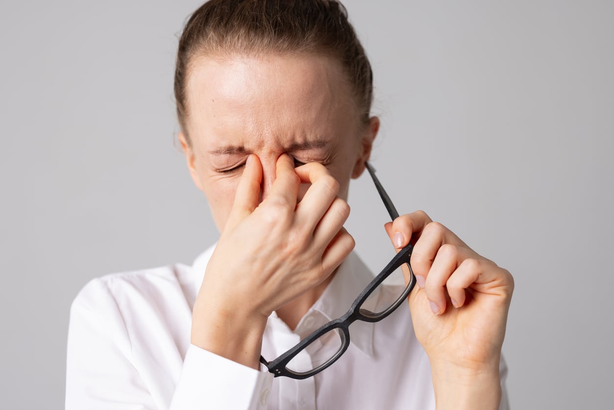 Woman with sinus pressure holding her nose bridge with glasses in the other hand